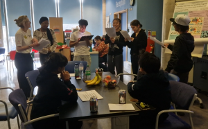 Young people stood round table reading out a script