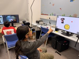 child sat with glasses on looking and pointing at a screen