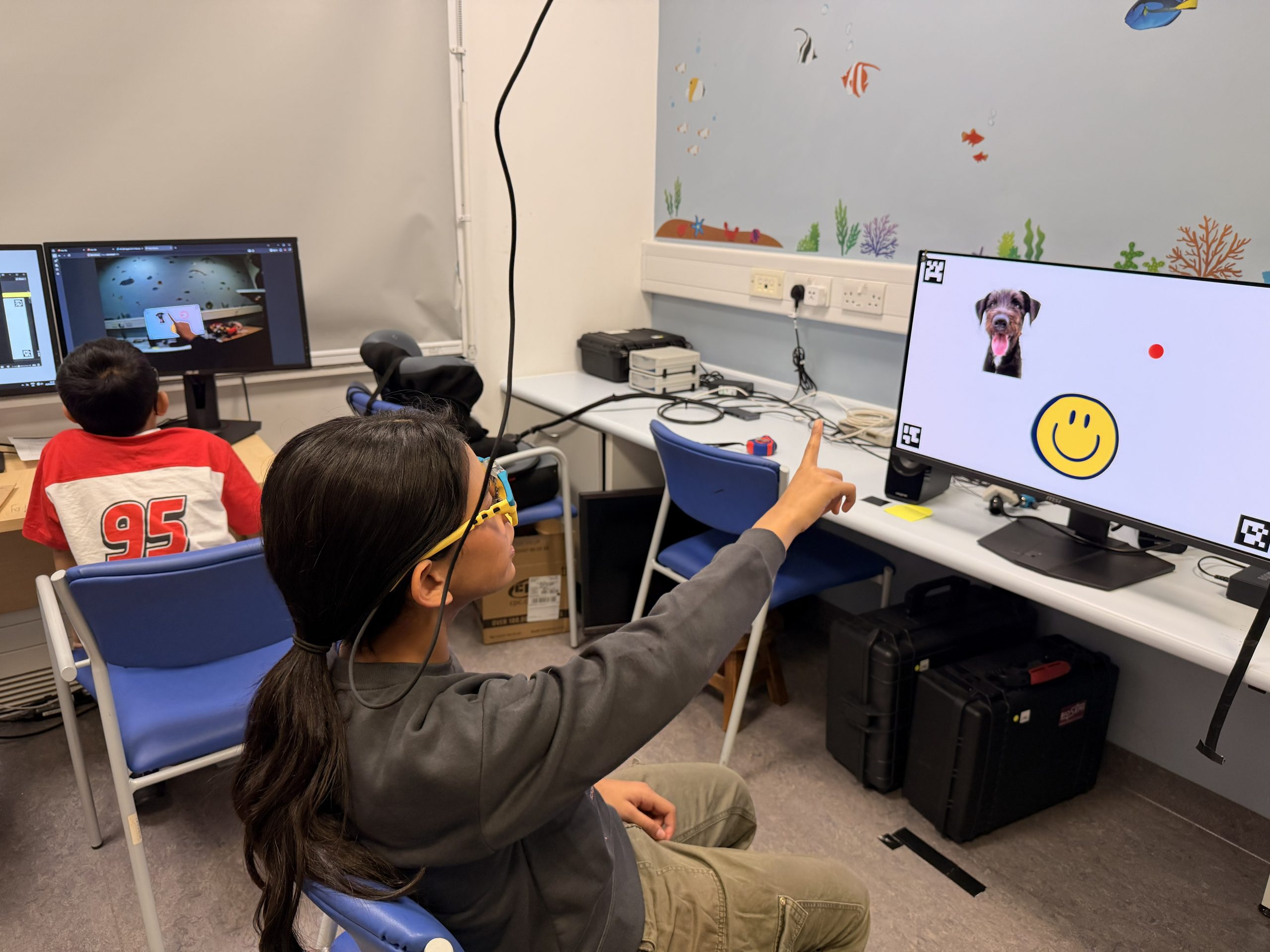 child sat with glasses on looking and pointing at a screen