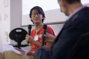 young person holding a microphone whilst doing an interview, person being interviewed blurred in foreground